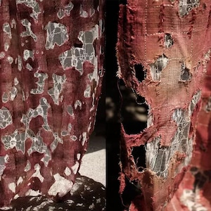 Könnte beinhalten: Nahaufnahme eines weinroten Stoffes mit einem zerfetzten, zerrissenen Aussehen. Der Stoff zeigt darunter ein weißes Spitzendesign, das einen geschichteten Effekt erzeugt. Die Kanten sind ausgefranst und die Gesamtstruktur ist rau und strukturiert.
