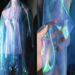 May include: Iridescent blue fabric with a shimmering, translucent quality. The fabric has a flowing drape, with hints of green and purple. The material appears lightweight and suitable for apparel or decorative purposes.