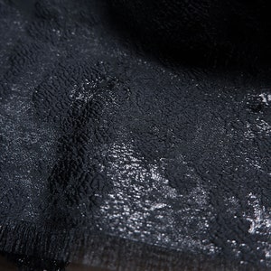 May include: Black scarf with a subtle shimmer and a textured pattern. The scarf has a fringed edge.