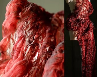 May include: A red, layered fabric design with a flowing, textured appearance. The fabric is draped and sculpted, creating a dynamic and artistic visual effect. The design is displayed on a mannequin, showcasing the intricate details and form.