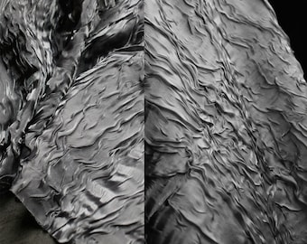 May include: Close-up of a silver fabric with a crinkled texture. The fabric is draped and folded, creating a wavy pattern.
