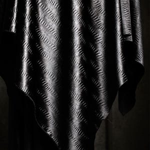 May include: Black fabric with a textured, embossed pattern. The fabric is draped and folded, creating a soft, flowing look.
