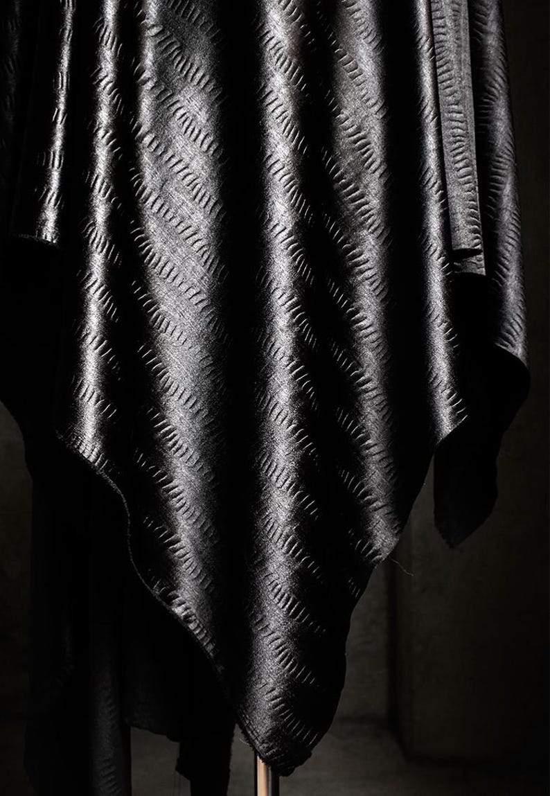 May include: Black fabric with a textured, embossed pattern. The fabric is draped and folded, creating a soft, flowing look.