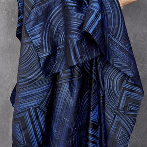 Puede incluir: Tela azul con un patrón geométrico de líneas y círculos negros. La tela está doblada y drapeada sobre una mano.