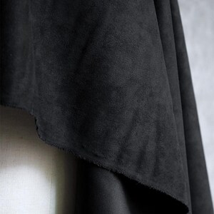 May include: Close-up of a draped piece of black fabric. The fabric has a soft, suede-like texture and a slightly uneven edge. The dark color and texture suggest it could be used for clothing or home decor.