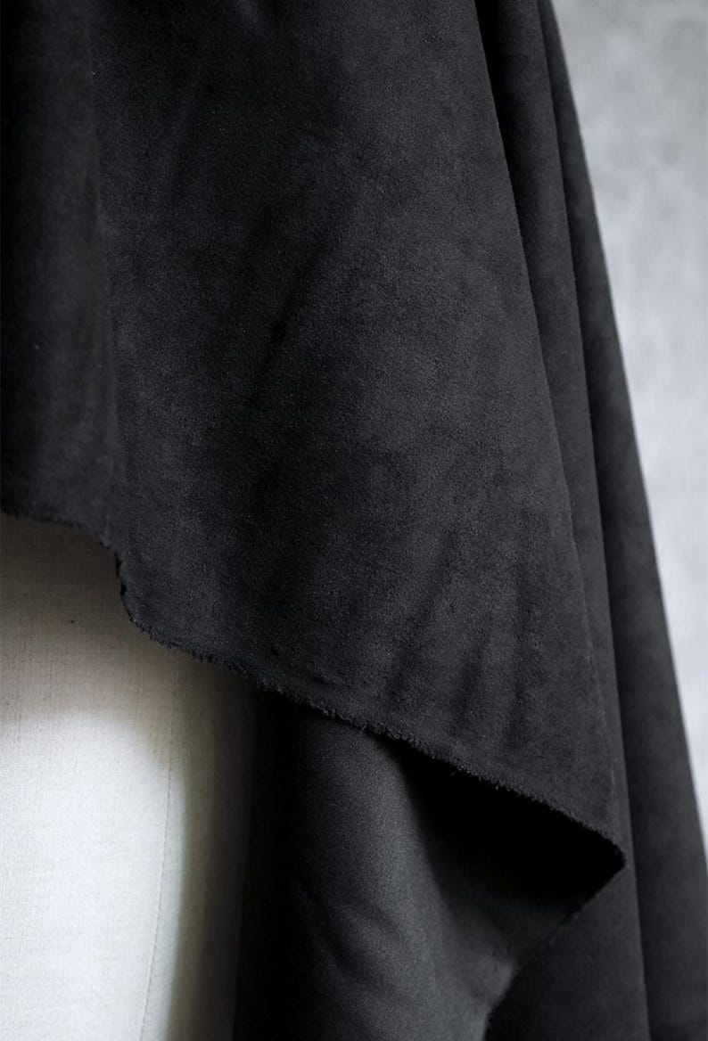 May include: Close-up of a draped piece of black fabric. The fabric has a soft, suede-like texture and a slightly uneven edge. The dark color and texture suggest it could be used for clothing or home decor.