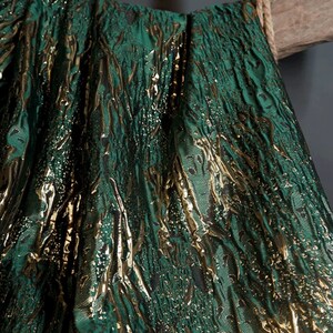 May include: Green fabric with a gold metallic pattern. The fabric has a textured, woven look.