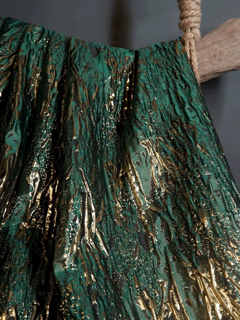 May include: Green fabric with a gold metallic pattern. The fabric has a textured, woven look.