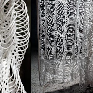 May include: White crocheted fabric with a delicate, intricate pattern. The fabric is woven in a way that creates a series of small holes, giving it a light and airy feel.