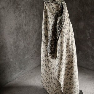 May include: A beige fabric with a black leaf pattern. The fabric is draped over a surface and has a dark green fabric underneath.