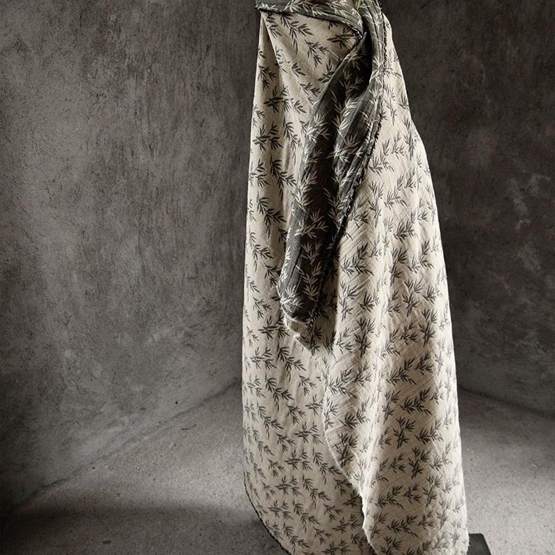 May include: A beige fabric with a black leaf pattern. The fabric is draped over a surface and has a dark green fabric underneath.
