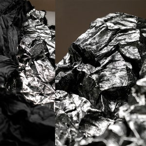 Puede incluir: Primer plano de una tela negra y plateada arrugada. La tela tiene un brillo metálico y una superficie texturizada.