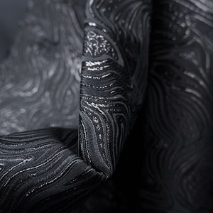 May include: Black fabric with a silver metallic swirl pattern. The fabric is textured and has a subtle sheen.