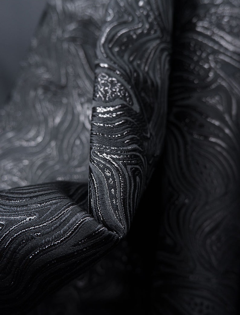 May include: Black fabric with a silver metallic swirl pattern. The fabric is textured and has a subtle sheen.
