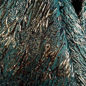 May include: Teal fabric with a gold metallic embossed pattern. The pattern resembles a series of abstract lines and shapes.