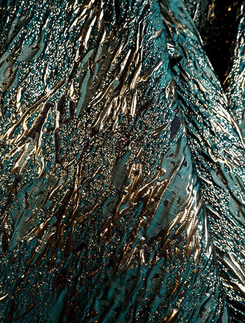 May include: Teal fabric with a gold metallic embossed pattern. The pattern resembles a series of abstract lines and shapes.