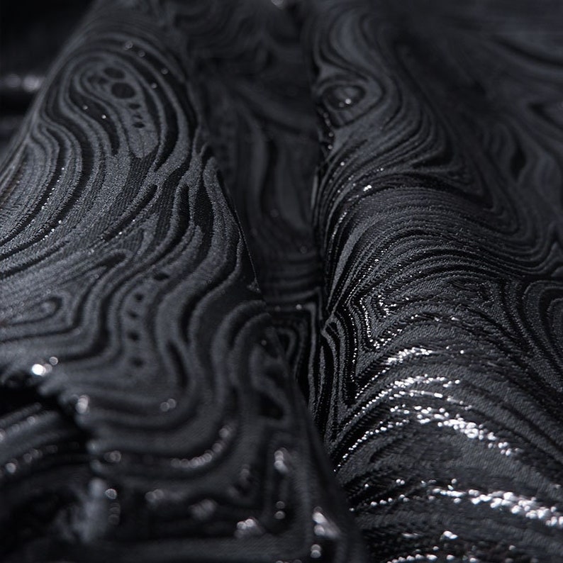 May include: Black fabric with a silver metallic swirl pattern. The fabric is textured and has a subtle sheen.