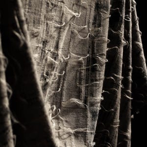 Puede incluir: Primer plano de una tela gris con textura deshilachada. La tela está doblada y drapeada, creando un patrón texturizado y abstracto.