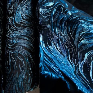 May include: Close-up of a textured fabric with a swirling, wave-like pattern. The fabric features a dark base color with shimmering blue highlights, creating a dynamic and iridescent effect. The design suggests a luxurious textile.