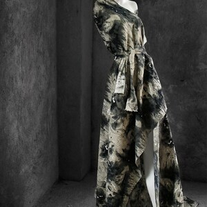 May include: A long, flowing dress with a black and white abstract print. The dress has a high neckline and a cinched waist with a black belt. The dress is made of a lightweight fabric and has a flowing silhouette.