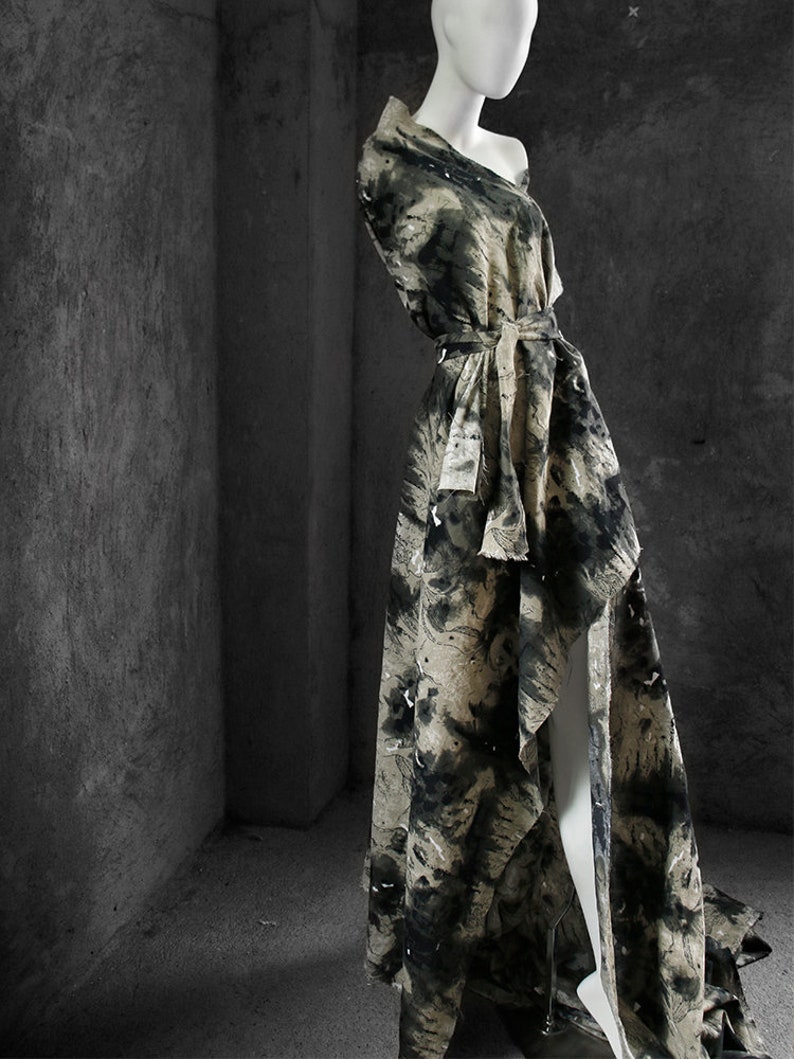 May include: A long, flowing dress with a black and white abstract print. The dress has a high neckline and a cinched waist with a black belt. The dress is made of a lightweight fabric and has a flowing silhouette.
