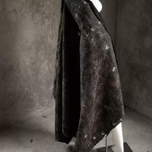 May include: A dark, textured fabric draped over a mannequin. The fabric appears to be a dark gray or black with lighter, irregular patches. The material hangs in soft folds, suggesting a garment or textile.