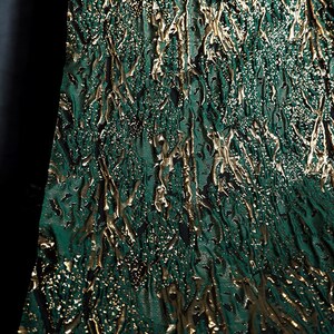 May include: Green fabric with a gold metallic pattern. The fabric has a textured, almost bark-like appearance.