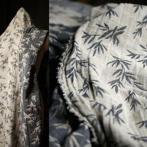 May include: A close-up of a beige fabric with a black bamboo leaf print. The fabric is folded and has a raw edge.