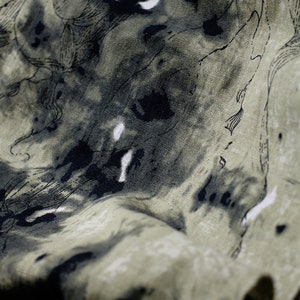 May include: A close-up of a green fabric with black ink splatter and a line drawing pattern. The fabric has a textured surface.