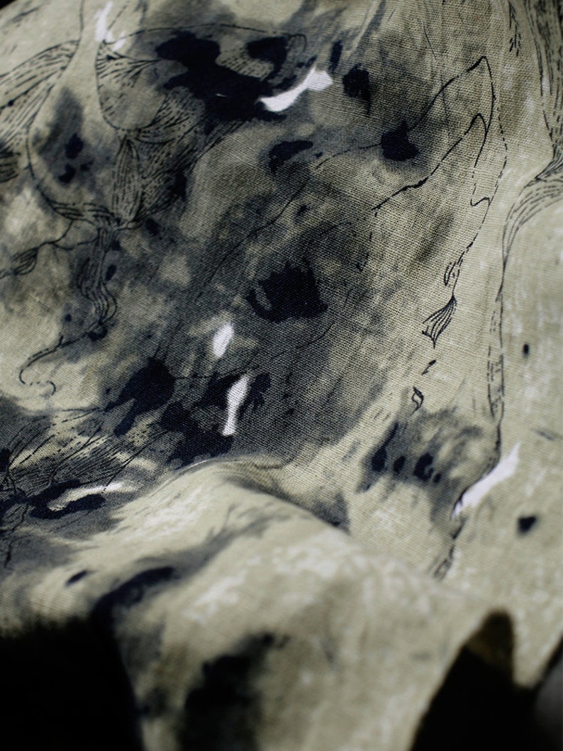May include: A close-up of a green fabric with black ink splatter and a line drawing pattern. The fabric has a textured surface.