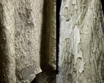 May include: Close-up of a flowing, light green fabric with a textured, distressed appearance. The fabric has a semi-sheer quality, with visible stitching and frayed edges. The overall aesthetic suggests a vintage or bohemian style.