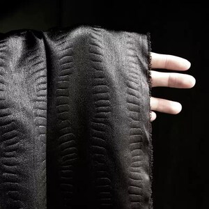May include: Black satin fabric with a textured, embossed pattern. The fabric has a subtle sheen and a soft, luxurious feel.