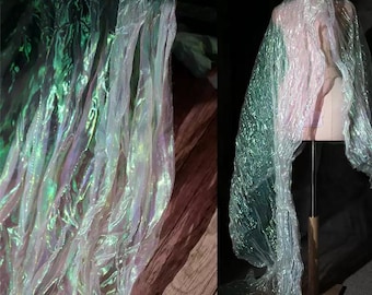 Peut inclure: Tissu irisé aux tons verts, blancs et roses. Le tissu est drapé sur un mannequin de couture et également présenté en gros plan. Le matériau a une qualité chatoyante et éthérée, suggérant un thème fantastique ou de costume.