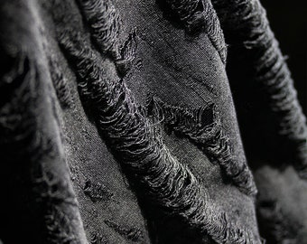 May include: Close-up of black fabric with a distressed, frayed texture. The fabric is wrinkled and has a rough, uneven surface.
