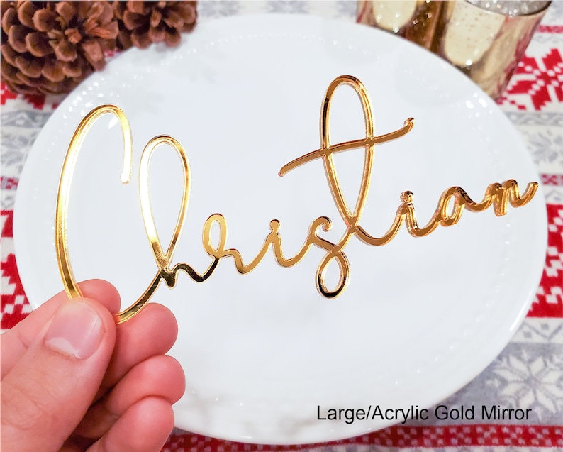 May include: Gold mirror acrylic place card with the name "Christian" written in a cursive script.