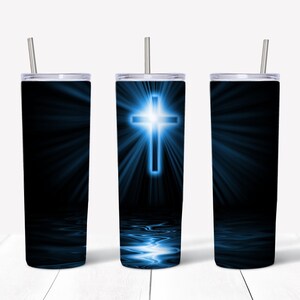 Könnte beinhalten: Drei Edelstahlbecher mit einem blauen Kreuzdesign. Das Kreuz leuchtet und ist von Lichtstrahlen umgeben. Der Hintergrund ist schwarz mit einer Reflexion des Kreuzes im Wasser am Boden des Bechers.