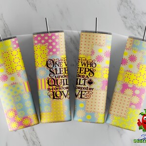 Peut inclure: Quatre gobelets isothermes en acier inoxydable avec couvercles et pailles. Chaque gobelet présente un motif patchwork jaune, rose et bleu, avec le texte "ONE WHO SLEEPS UNDER A QUILT IS COMFORTED BY LOVE". Les gobelets sont cylindriques.