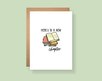 May include: A white greeting card with a brown envelope featuring a stack of colorful books and the black text "HERE'S TO A NEW chapter". The illustration shows an open book resting on top of several closed books in shades of red, blue, and yellow.