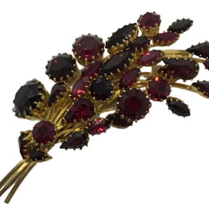 Peut inclure: Une broche dorée avec un groupe de strass rouges et noirs en forme de fleur.