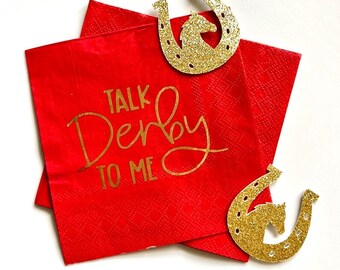 May include: Two red paper napkins with gold glitter horseshoes and the text "Talk Derby To Me" printed on them.