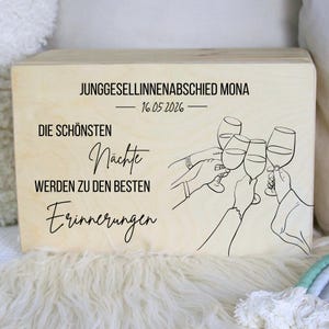 Könnte beinhalten: Eine rechteckige, helle Holzbox mit einer schwarzen Strichzeichnung von vier Händen, die Weingläser zum Anstoßen halten. Der Text lautet JUNGGESELLINNENABSCHIED MONA, 16.05.2026, DIE SCHÖNSTEN Nächte WERDEN ZU DEN BESTEN Erinnerungen.