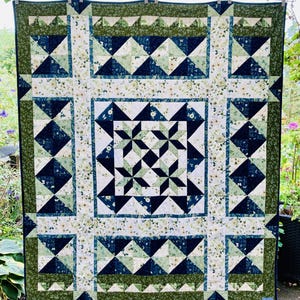 Puede incluir: Un edredón grande con un diseño de patchwork. El edredón presenta un cuadrado central con un patrón de estrella, rodeado de formas geométricas en tonos azules, verdes y blancos. La etiqueta "QUILT B" es visible en la parte superior.