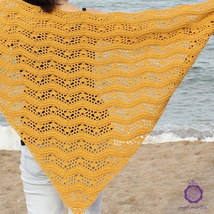 Puede incluir: Un chal de crochet amarillo con un patrón de ondas. El chal está drapeado sobre los hombros de una persona y se está usando al aire libre.