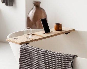 May include: A white bathtub with a wooden bath tray, a glass, a smartphone, and a wooden cup. A gray waffle weave towel hangs over the side of the tub.