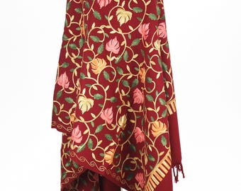 May include: A maroon shawl with intricate floral embroidery in shades of pink, yellow, and green. The shawl has a fringed border and is draped over a mannequin.