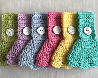 May include: Six crocheted dishcloths in various pastel colors, each with a white button in the center. The dishcloths are arranged in a row from left to right, with the green dishcloth on the left and the turquoise dishcloth on the right.