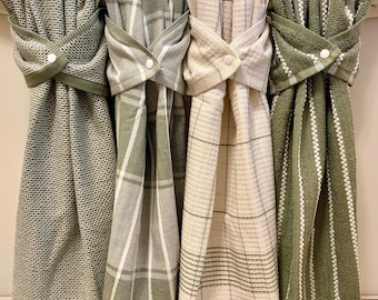 May include: Four hanging kitchen towels featuring a snap button closure at the top. The set includes one solid sage green waffle weave towel, one sage green and white plaid towel, one cream and sage plaid towel, and one sage green striped towel.