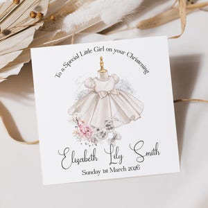 May include: A square card with a watercolor illustration of a baby dress on a dress form. The card reads "To a Special Little Girl on your Christening" and includes the name "Elizabeth Lily Smith" and the date "Sunday 1st March 2026".