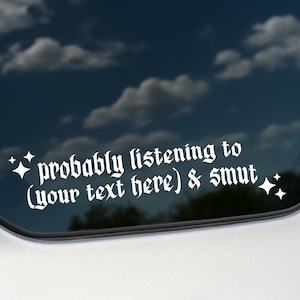 May include: White vinyl decal for a car window. The text reads "probably listening to (your text here) & smut" in a gothic font, with starburst accents. The decal is on a silver vehicle with a blue sky background.