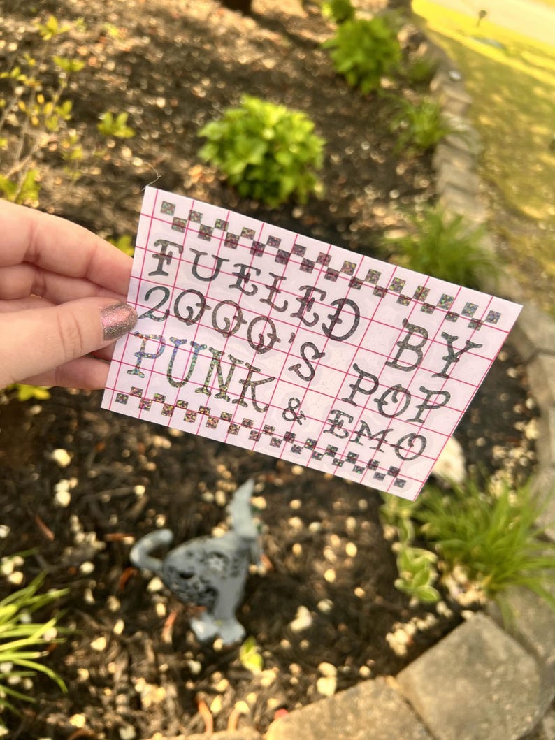 May include: A white piece of paper with a grid pattern and the text "Fueled by 2000's Pop Punk & Emo" written in black ink.